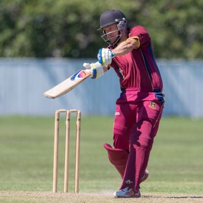 A person in a red uniform playing cricket
Description automatically generated